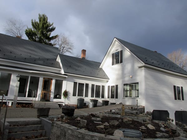 Historic 1897 white farmhouse in Merrimack NH with Interlock deep charcoal aluminum slate metal roofing across multiple gabled roof sections.