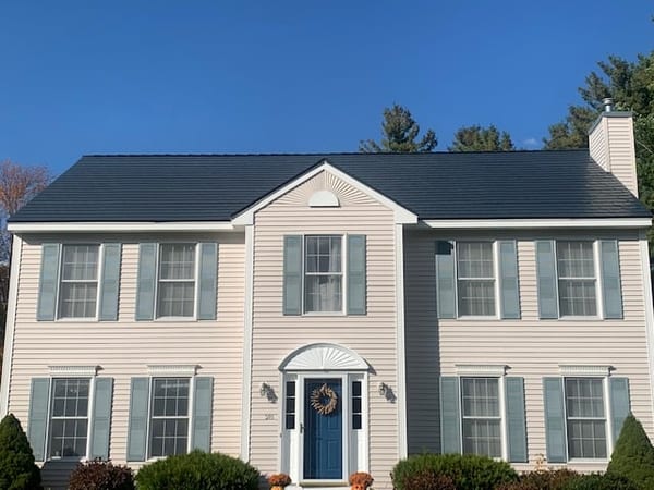 Two-story Colonial home in Merrimack NH with Interlock deep charcoal aluminum slate metal roof, dark shutters, and blue front door.