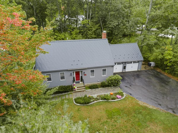 Black Interlock Slate aluminum roof on a grey single-family home with a metal roof among trees, Rochester, New Hampshire