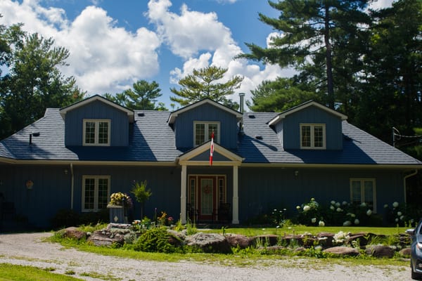 Front elevation of a blue board-and-batten home in Washago, ON with Interlock charcoal grey aluminum slate roofing, three dormers, and a covered entry porch.