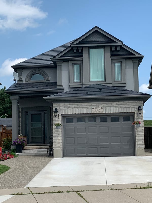 Two-storey Colonial home in Cambridge ON with black Interlock aluminum slate metal roof, complex multi-hip profile, dormer, and grey stucco and stone exterior.
