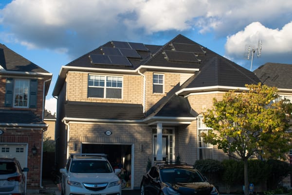 Two-storey suburban home in Oakville ON with black Interlock aluminum slate metal roof featuring multiple solar panels across a complex multi-hip roofline.