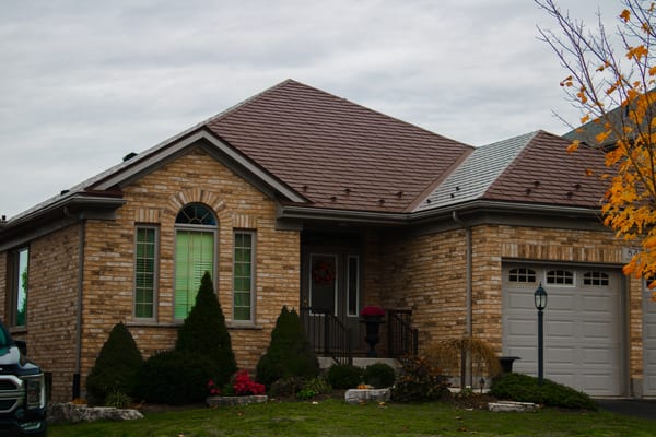 Single-storey brick ranch home with Interlock aluminum slate roof in Colonial Brown, featuring a multi-hip roofline, arched entry window, and attached garage.