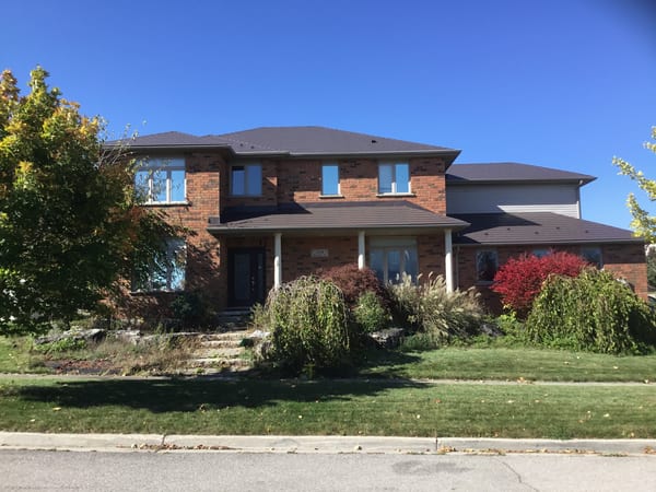 Two-storey brick home in Cambridge ON with Interlock Tudor Brown aluminum slate metal roof across multi-hip rooflines, set against a clear blue autumn sky.
