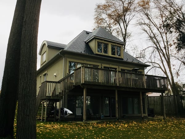 Rear elevation of a 3-storey Victorian home in Orillia ON featuring black Interlock aluminum slate roofing with a central turret, dormer, and large elevated wood deck.