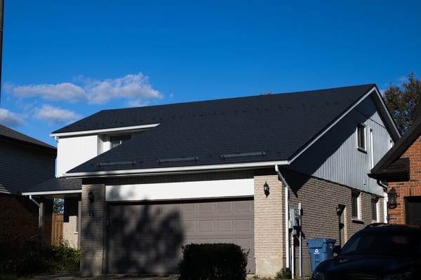 Two-storey suburban home in Guelph, ON with a deep charcoal Interlock aluminum slate metal roof featuring snow rails, under a bright blue sky.