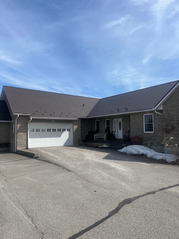 Single-storey brick ranch home in Innisfil, ON with Interlock Tudor Brown cedar shingle metal roof, wide driveway, and attached garage in winter.