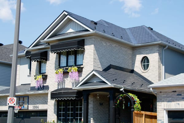 Two-storey suburban home in Milton, ON with a complex multi-hip black Interlock aluminum slate metal roof, snow guards, black awnings, and wisteria window boxes.
