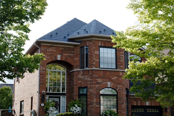 Two-storey brick home in Scarborough with a complex turreted Interlock aluminum slate roof in deep charcoal, featuring snow guards and multi-hip planes.