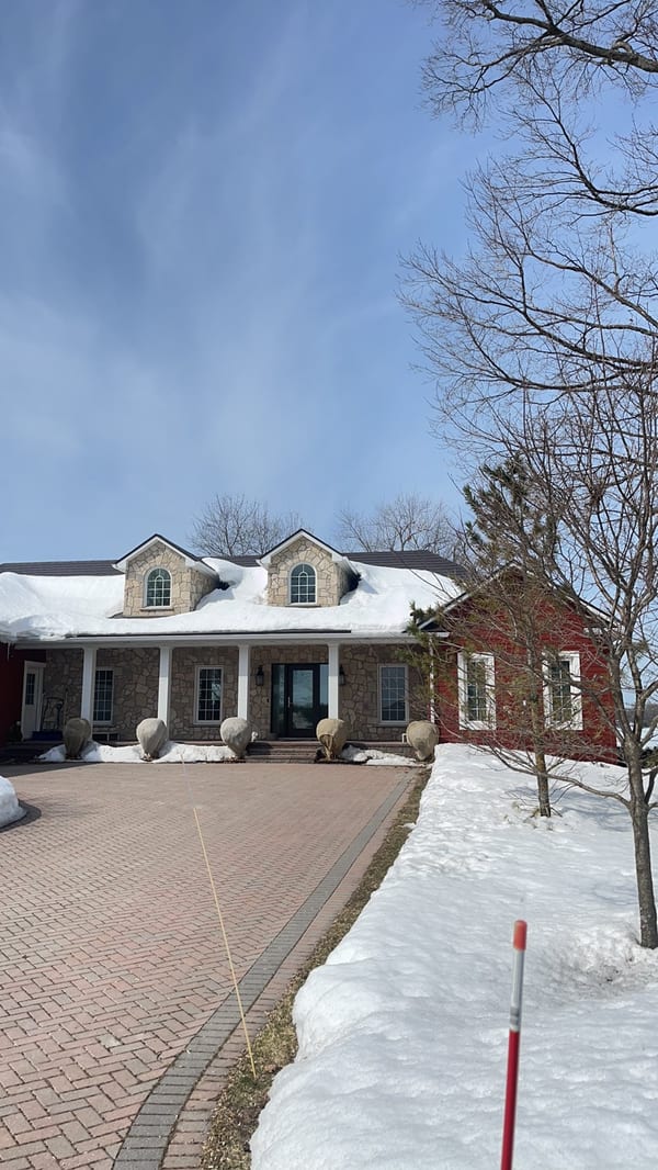Tudor Brown Interlock aluminum slate roof with twin dormers on a 1.5-storey stone Colonial home in Orillia, ON, photographed in winter.