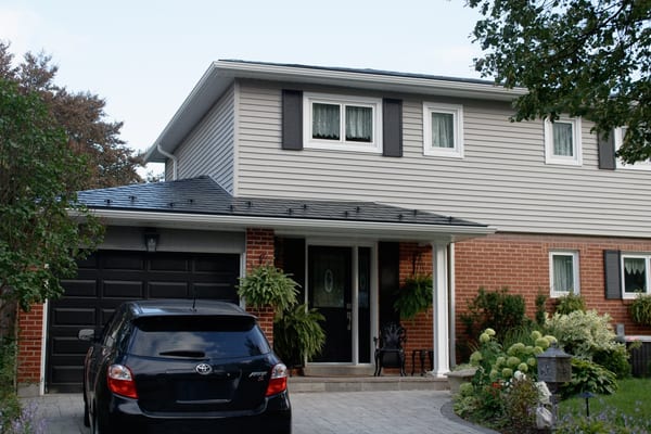 Two-storey brick and vinyl-sided Colonial home in Scarborough with black Interlock aluminum slate metal roofing on a hip-style roof.