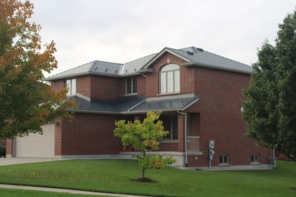 Two-storey red brick Colonial home in Cambridge, ON with a complex multi-hip deep charcoal Interlock aluminum cedar shingle metal roof.