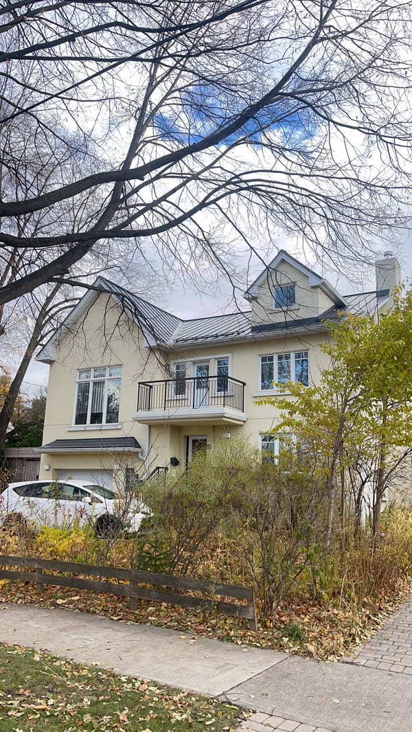 Two-storey Etobicoke home with deep charcoal standing seam metal roof featuring dormers and complex multi-plane roofline, photographed from street in autumn.