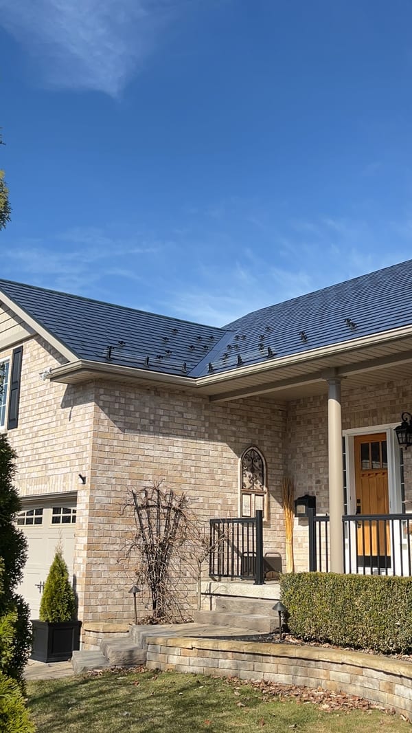Black Interlock aluminum slate metal roof on a two-storey brick Colonial home in Cobourg, ON, featuring snow guards and complex multi-hip rooflines.