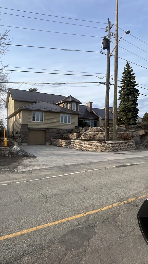 Two-storey craftsman home in Sudbury ON with Interlock Colonial Brown slate metal roofing, multi-hip complex roof, stone retaining walls, and turret feature.