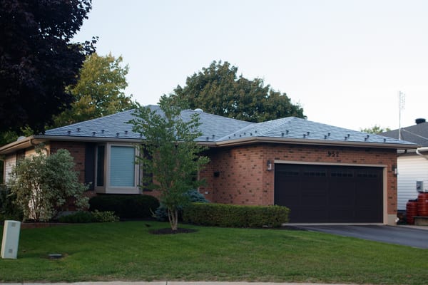 Single-storey ranch-style brick home with a low-hip Interlock aluminum slate roof in Colonial Brown, featuring snow guards and a double dark garage door.