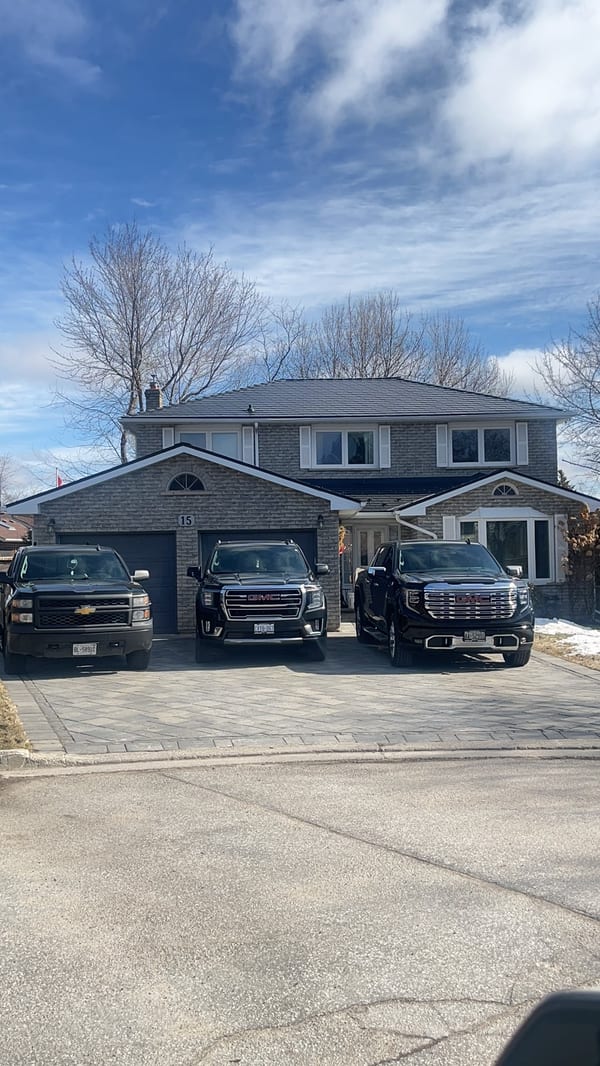 Two-storey brick Colonial home in Bradford, ON with black Interlock aluminum slate metal roofing, double garage, and three black trucks in the driveway.