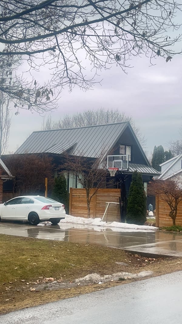 Steep A-frame home with Interlock Musket Grey standing seam metal roof, cedar fence, and basketball hoop in a suburban Burlington neighbourhood.