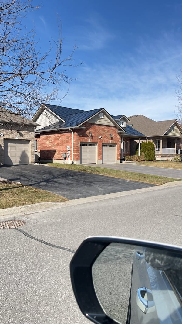 Street-view of a brick semi-detached home in Cobourg, ON featuring a black Interlock aluminum slate metal roof with multi-hip profile.