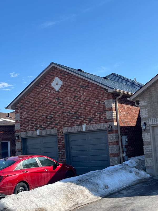Deep charcoal Interlock aluminum slate metal roof on a two-storey red brick home with double garage, photographed in winter in Barrie, ON.