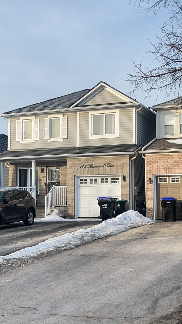 Two-storey suburban home at 142 Maplewood Drive, Angus ON, with black Interlock aluminum slate metal roofing on a medium-pitch gable, tan vinyl siding, and brick facade.