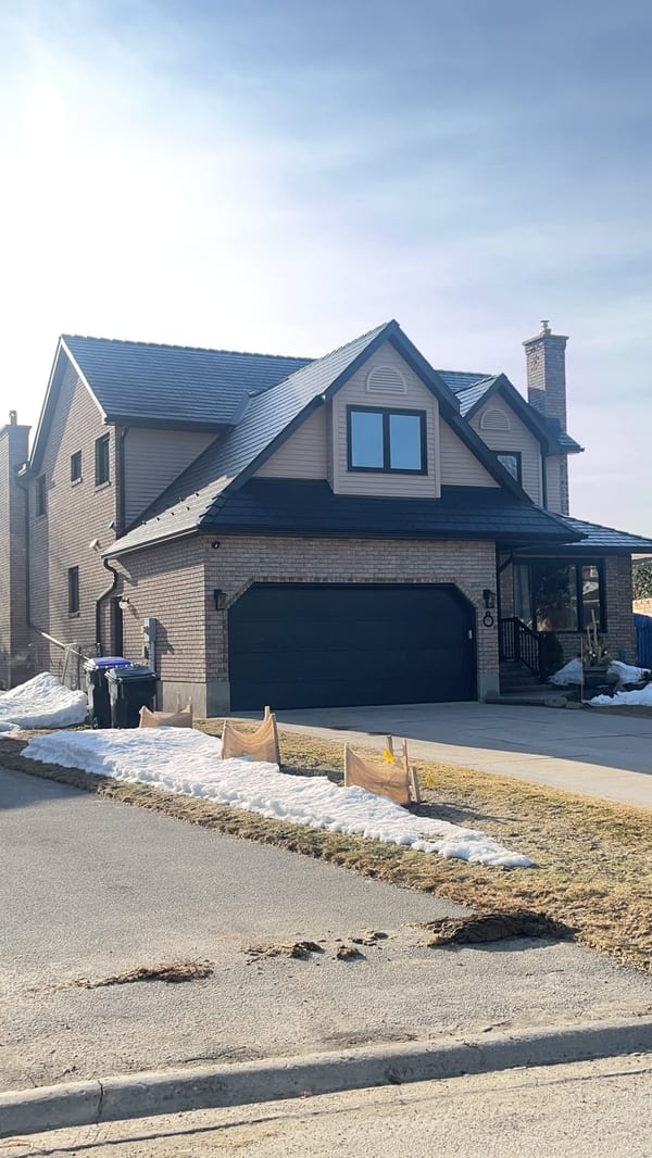 Two-storey Craftsman home in Collingwood ON with black Interlock aluminum slate metal roof, prominent dormer, and brick facade photographed in winter.