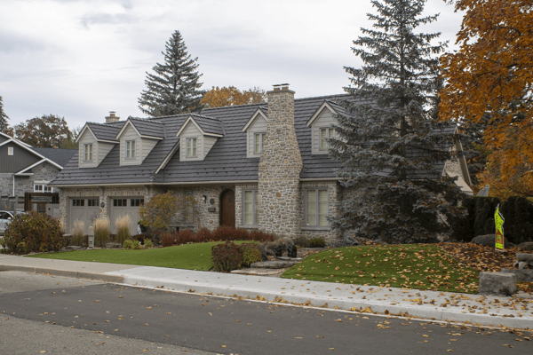 Tudor-style stone home in Waterloo ON with Interlock aluminum shake roofing in Tudor Brown, featuring multiple dormers and a prominent stone chimney.