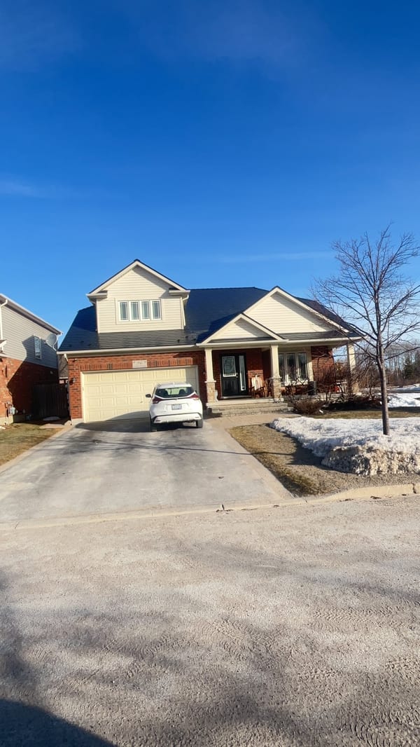 1.5-storey Craftsman home in Collingwood ON with black Interlock aluminum slate metal roof, front dormer, and brick facade on a clear winter day.