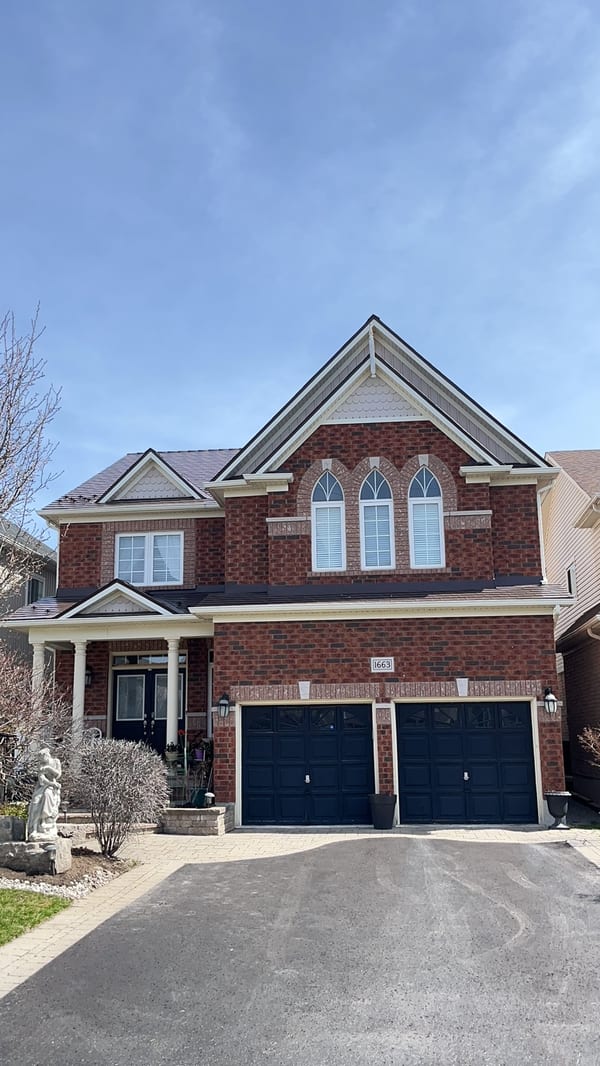 Two-storey brick Colonial home in Oshawa with Interlock aluminum slate roof in Colonial Brown, featuring multi-gable roofline and double navy garage doors.