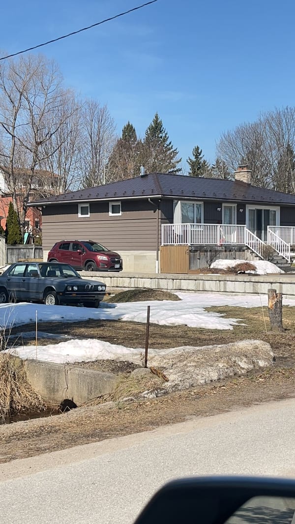 Single-storey ranch home with Interlock Colonial Brown aluminum slate metal roof on a hip profile, chimney visible, photographed in early spring.