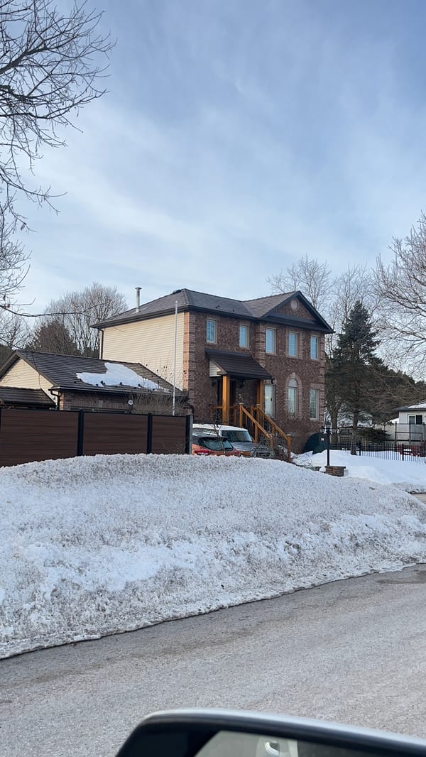 Two-storey brick Colonial home in Angus ON with Interlock Colonial Brown slate metal roof, multi-hip profile, viewed from street in winter.