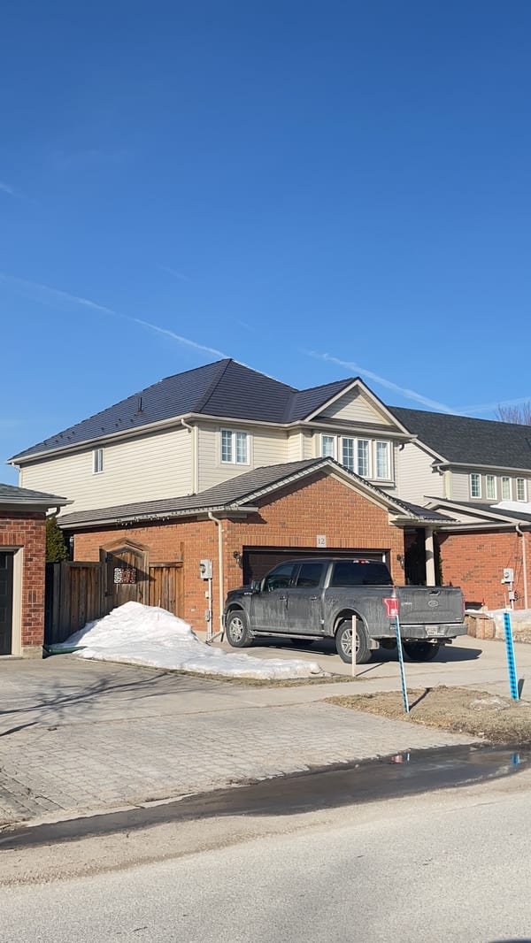 Two-storey brick home in Collingwood, ON with a complex hip roof clad in Interlock Tudor Brown aluminum slate roofing under a clear blue winter sky.