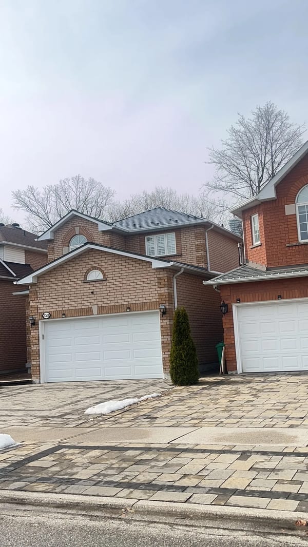 Black Interlock Slate aluminum roof on a two-storey red brick home with white trim among suburban, Mississauga, Ontario