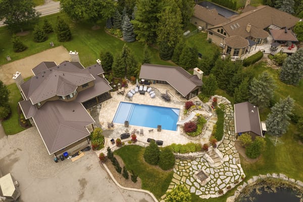 Aerial view of a large Craftsman-style home in Bradford, ON featuring Interlock Tudor Brown aluminum slate metal roofing with complex multi-hip roof and poolside estate.