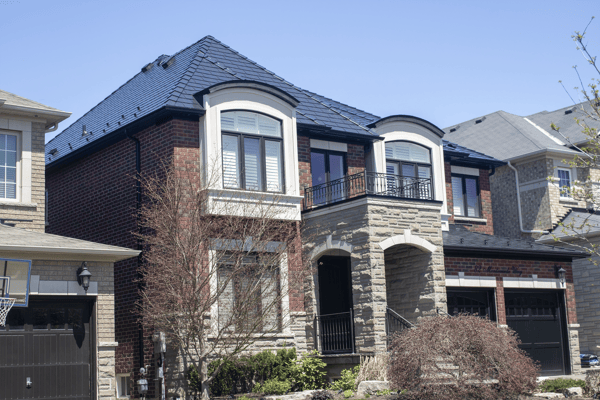 Two-storey brick and stone Colonial home in Woodbridge, ON with a complex multi-hip black Interlock aluminum slate metal roof and wrought-iron balcony.