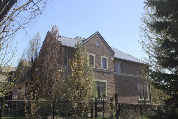 Two-storey Tudor-style brick home in Woodbridge ON with Interlock black aluminum slate metal roofing featuring steep gabled dormers and multi-plane roof.