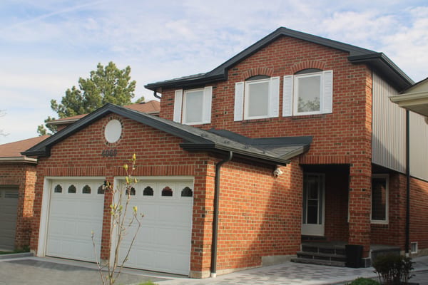 Two-storey red-brick Colonial home in Mississauga with Interlock Deep Charcoal aluminum slate roofing, multi-hip complex roofline, and double white garage doors.