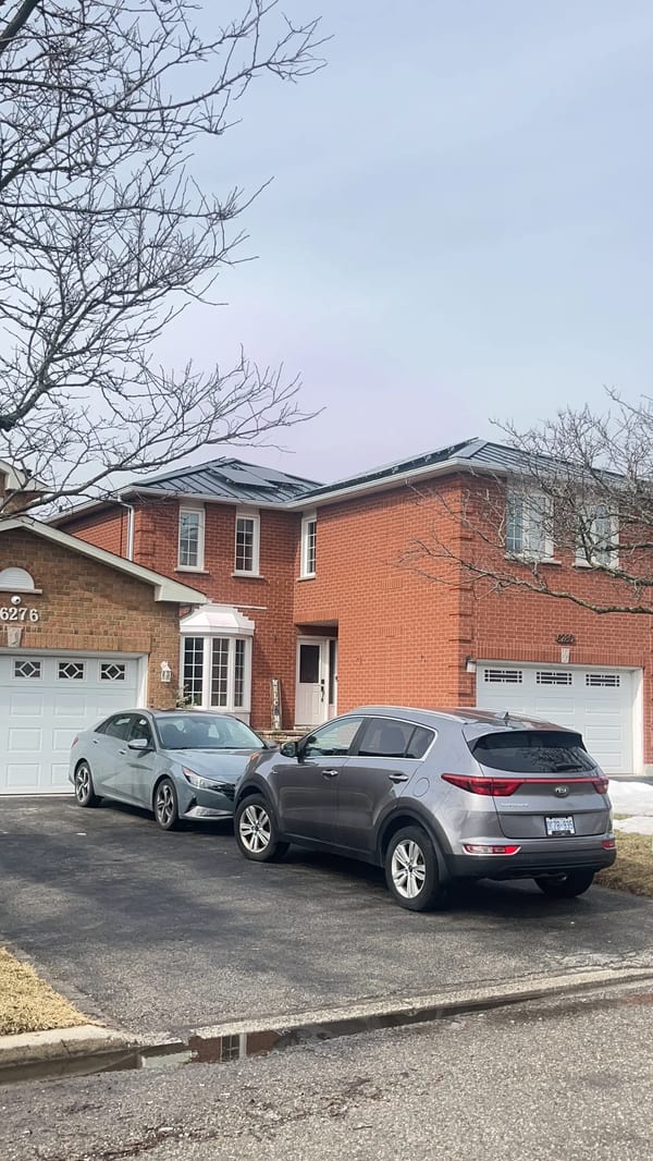 Black Interlock Standing Seam aluminum roof on a two-storey brick home with a metal roof among tall trees, Mississauga, Ontario