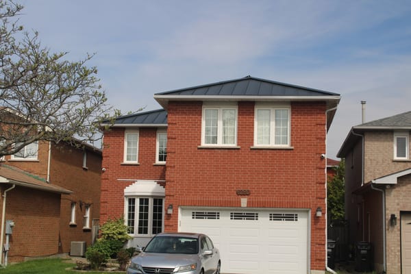 Two-storey red brick home in Mississauga with a low-pitch hip roof finished in black Interlock aluminum standing seam metal roofing.
