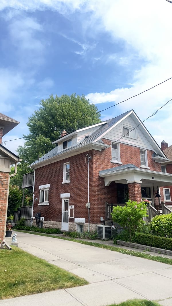Two-storey red brick home in Kitchener ON featuring Interlock deep charcoal aluminum slate metal roofing with dormer and covered front porch.