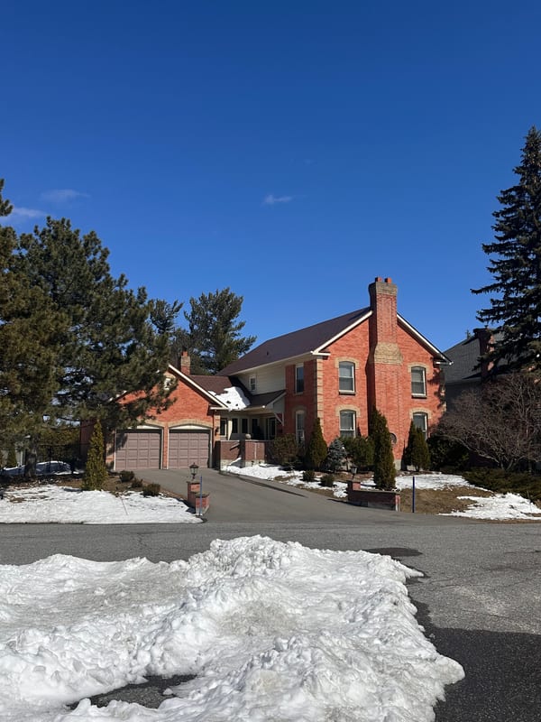 Two-storey red brick colonial home in Stittsville ON with Interlock Tile Red aluminum slate metal roof and prominent chimney, photographed in winter.