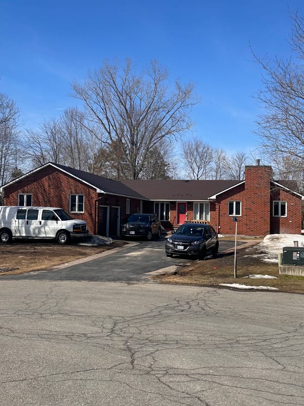 Front elevation of a single-storey red brick ranch home in Navan, ON featuring an Interlock Colonial Brown aluminum shingle roof with hip lines and prominent chimney.