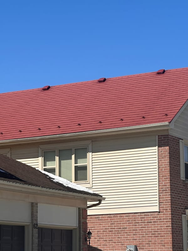 Tile red Interlock aluminum shingle metal roof on a 2-storey brick and vinyl colonial home in Stittsville, ON, under a clear blue sky.