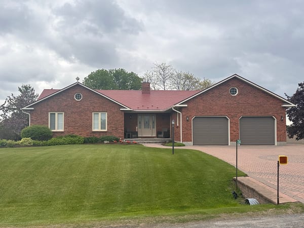 Front elevation of a brick ranch home with Interlock Tile Red aluminum shingle metal roof, dual gable peaks, chimney, and double garage in North Gower, ON.