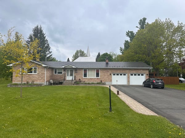 Front elevation of a single-storey ranch-style brick home in North Gower, ON, featuring a low-pitch black Interlock aluminum slate metal roof with chimney.