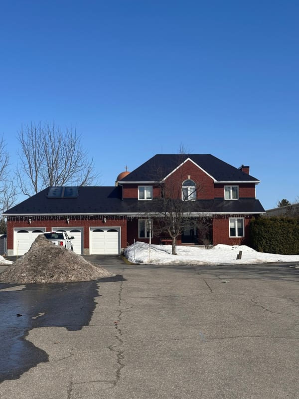 Two-storey red brick Colonial home in Navan ON with black Interlock aluminum slate roofing, turret, skylights, and triple-car garage in winter.