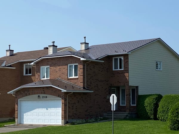 Two-storey brick home in Orleans ON with Interlock Colonial Brown aluminum slate metal roofing across a complex multi-hip roof, viewed from the street.