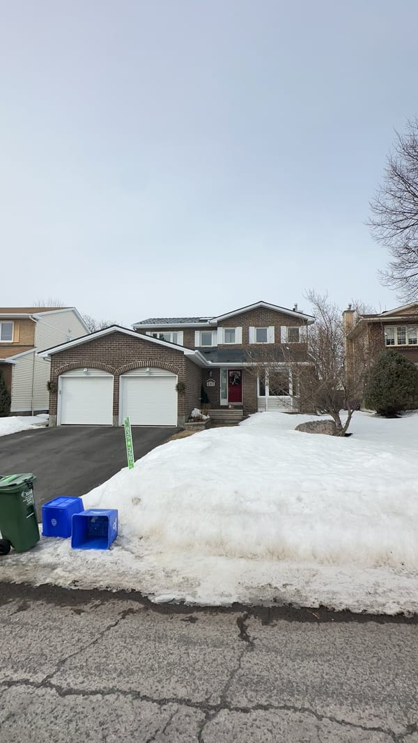 Two-storey brick home in Orleans ON with Interlock deep charcoal aluminum slate metal roof, double garage, shot from across snowy street.