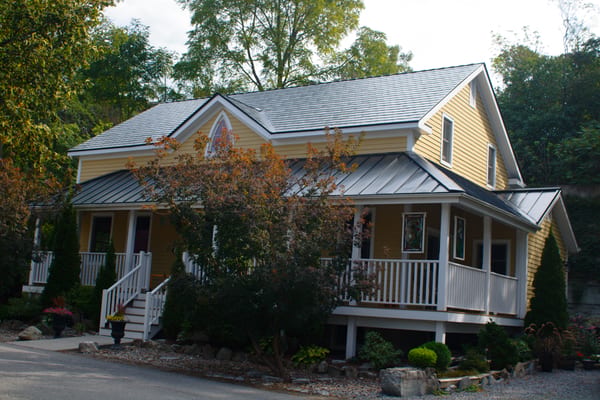 Yellow Craftsman home in Kingston ON featuring a black Interlock aluminum slate metal roof with complex multi-hip profile, white porch railings, and dormer.