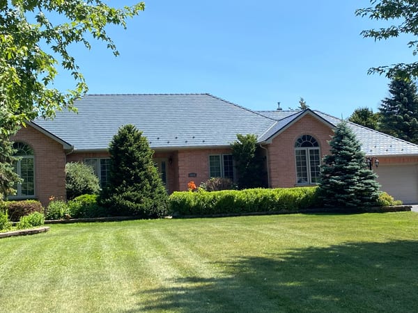 Deep Charcoal Interlock Slate aluminum roof on a brick home with a metal roof and green shrubs in a, Cornwall, Ontario